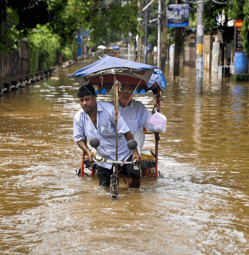 Flood-affected community navigating through floodwaters in Assam during the 2026 monsoon floods